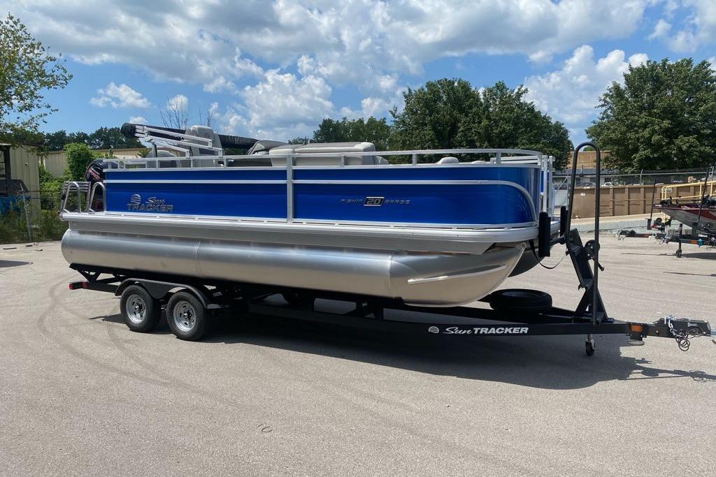 2026 Sun Tracker Fishin' Barge 20 DLX pontoon boat on trailer under blue sky.