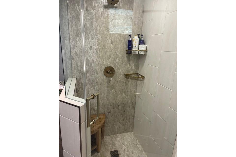 Modern shower with glass door, tiled walls, and corner shelf in Adonia's 2021 Queen Elizabeth model.
