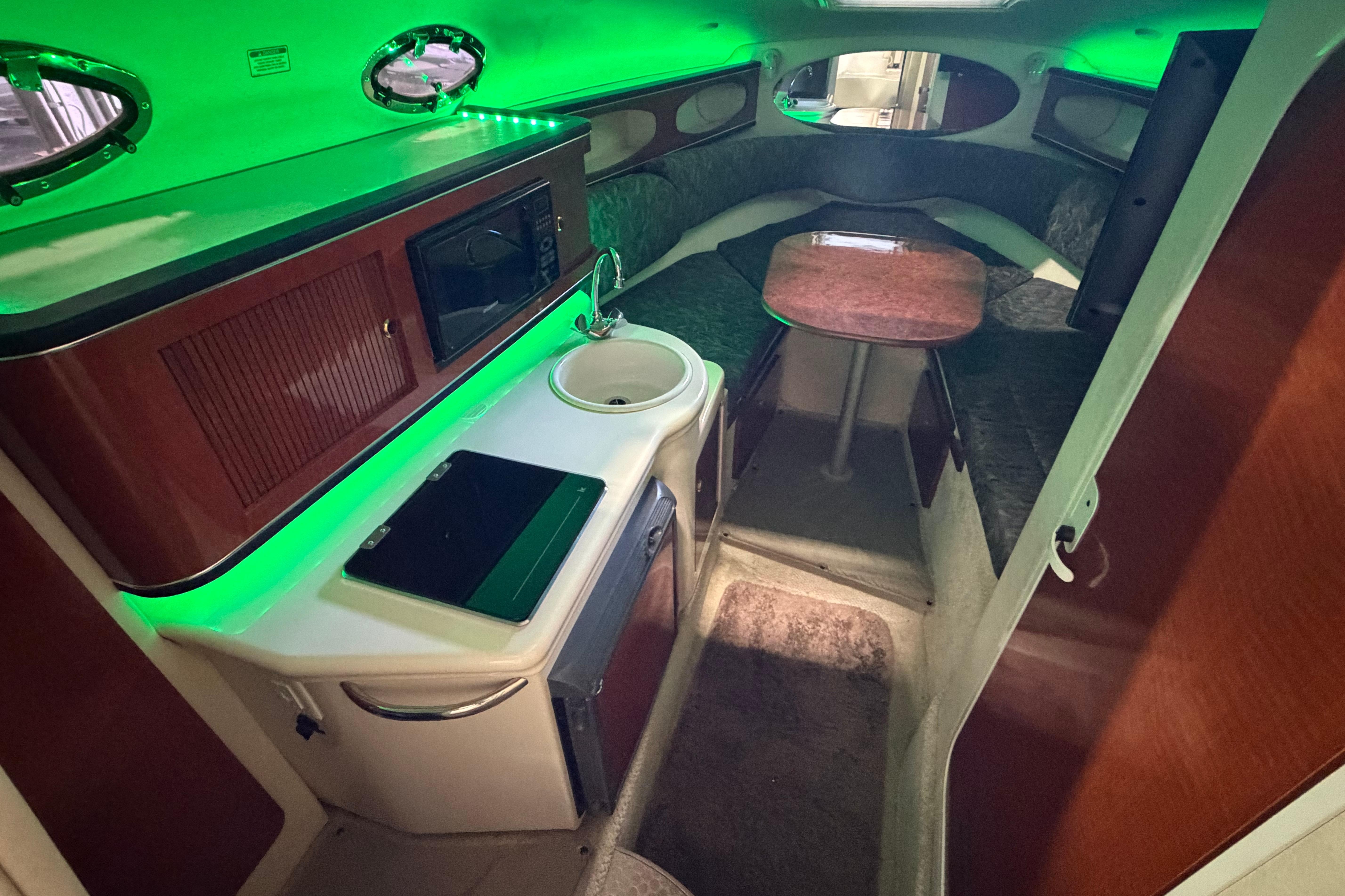 Interior of 2004 Sea Ray Sundancer 260 with kitchenette and seating area, illuminated by green lighting.