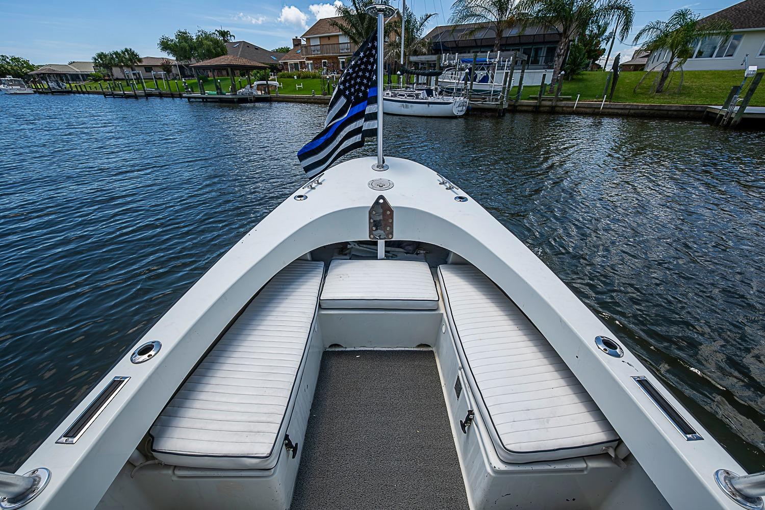 1969 custom boat with white seating, blue-striped flag, docked in a scenic waterfront area.