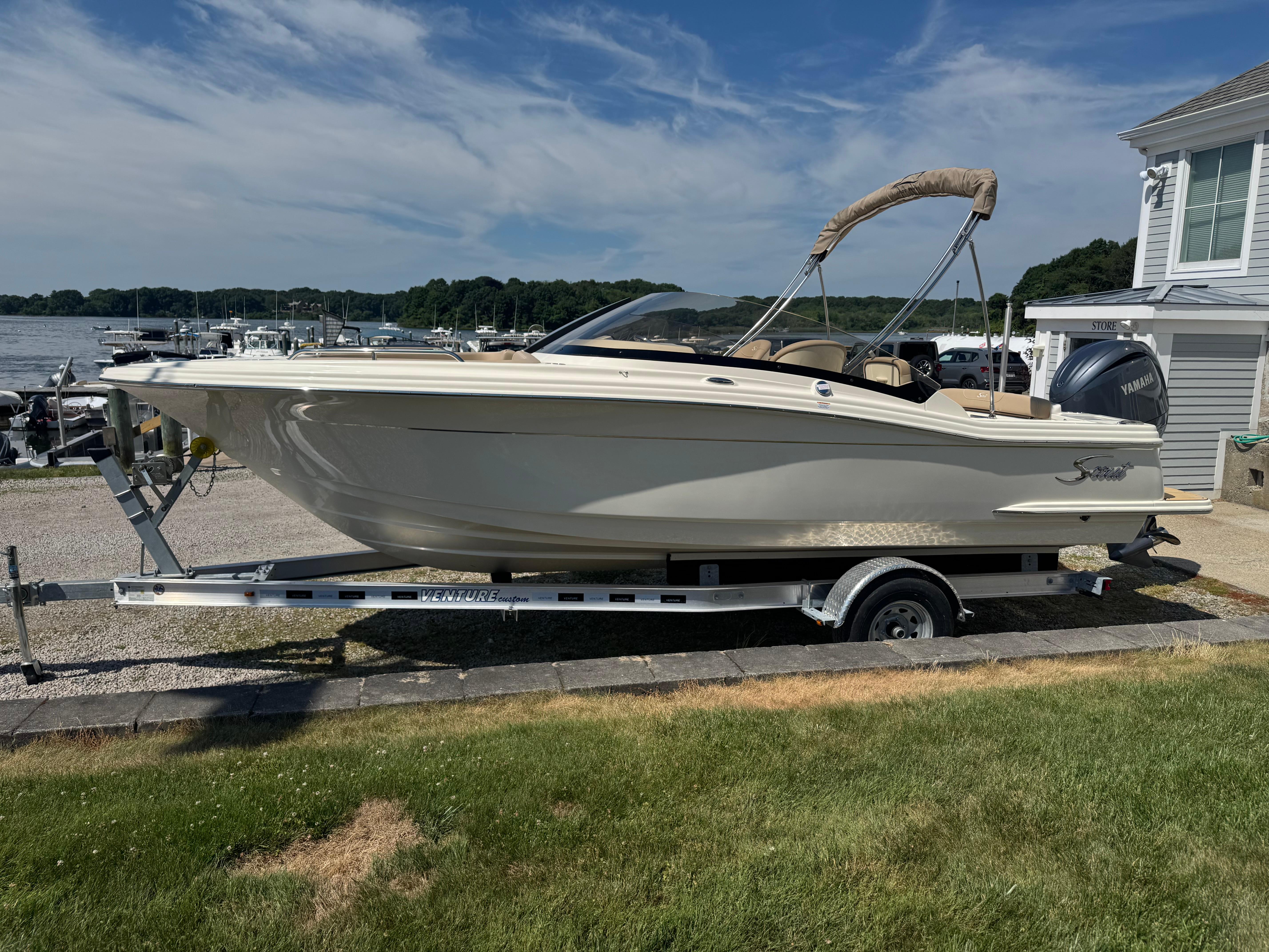 2025 Scout 215 Dorado boat on trailer, parked near waterfront, under clear blue sky.