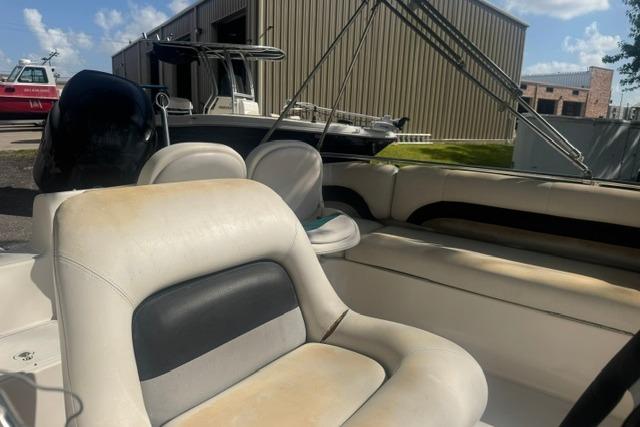1999 Hurricane SunDeck Sport 201 OB boat interior with beige seating, docked near a warehouse.