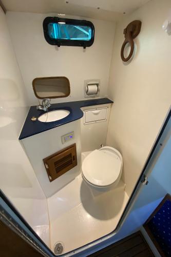 Interior view of a boat bathroom with toilet, sink, and porthole.