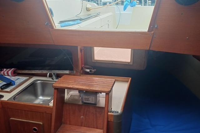Interior of 1989 O'Day 272 sailboat with wooden cabinetry and compact kitchen area.