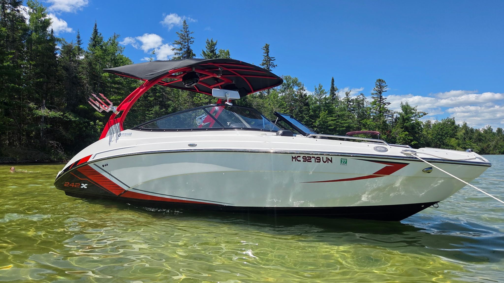 A 2018 Yamaha 242X E-Series boat floats on clear water, surrounded by trees.