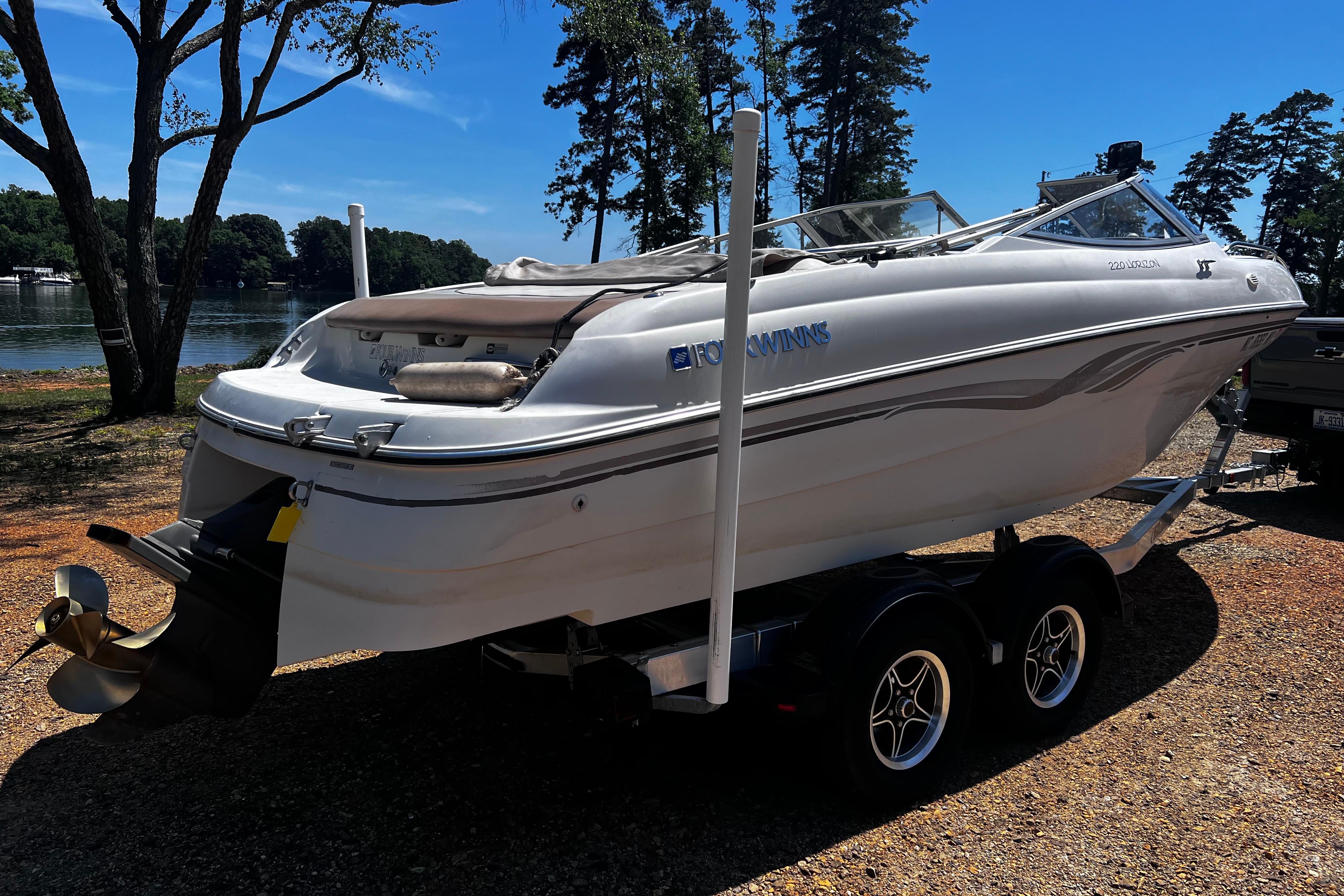 1998 Four Winns 220 Horizon boat on trailer by a lakeside, under clear blue sky.