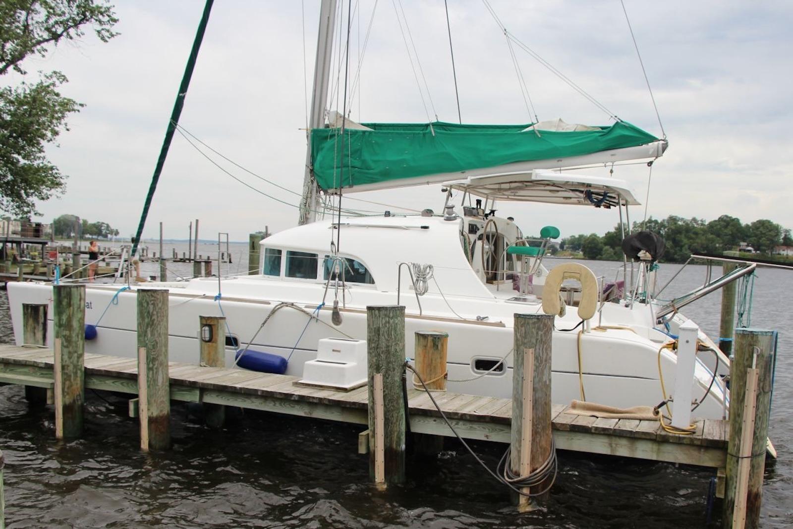 2004 Lagoon 380 catamaran docked at a marina with green sail cover.