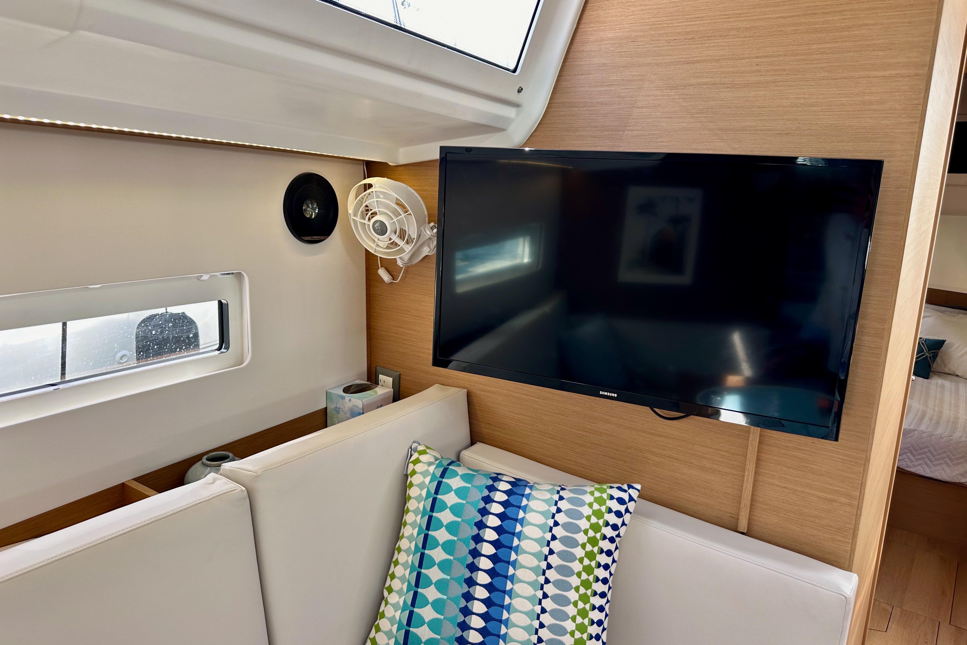 2024 Jeanneau Sun Odyssey 410 interior with TV, fan, and colorful cushion.