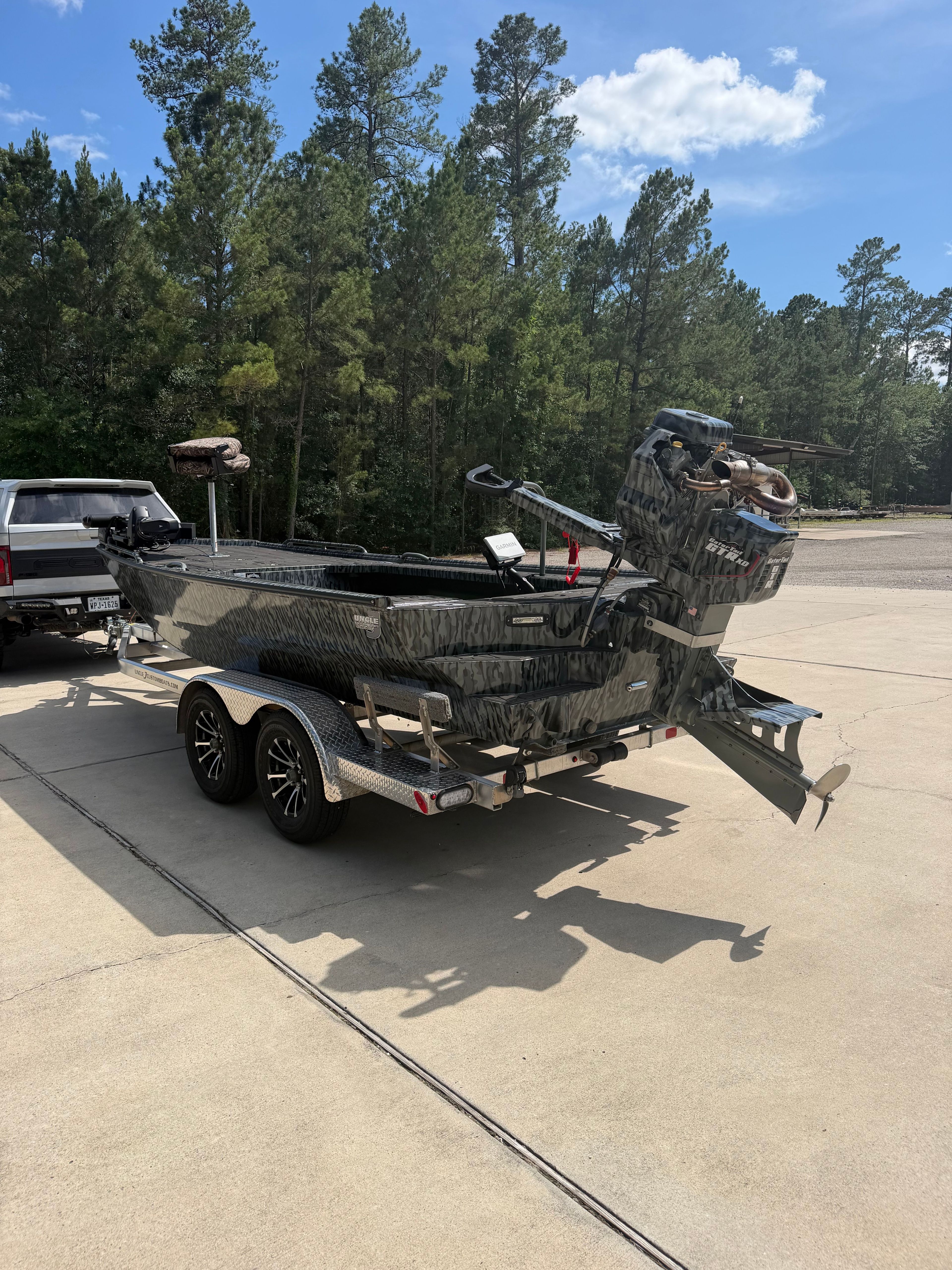 A boat on a trailer surrounded by trees, featuring an outboard motor.