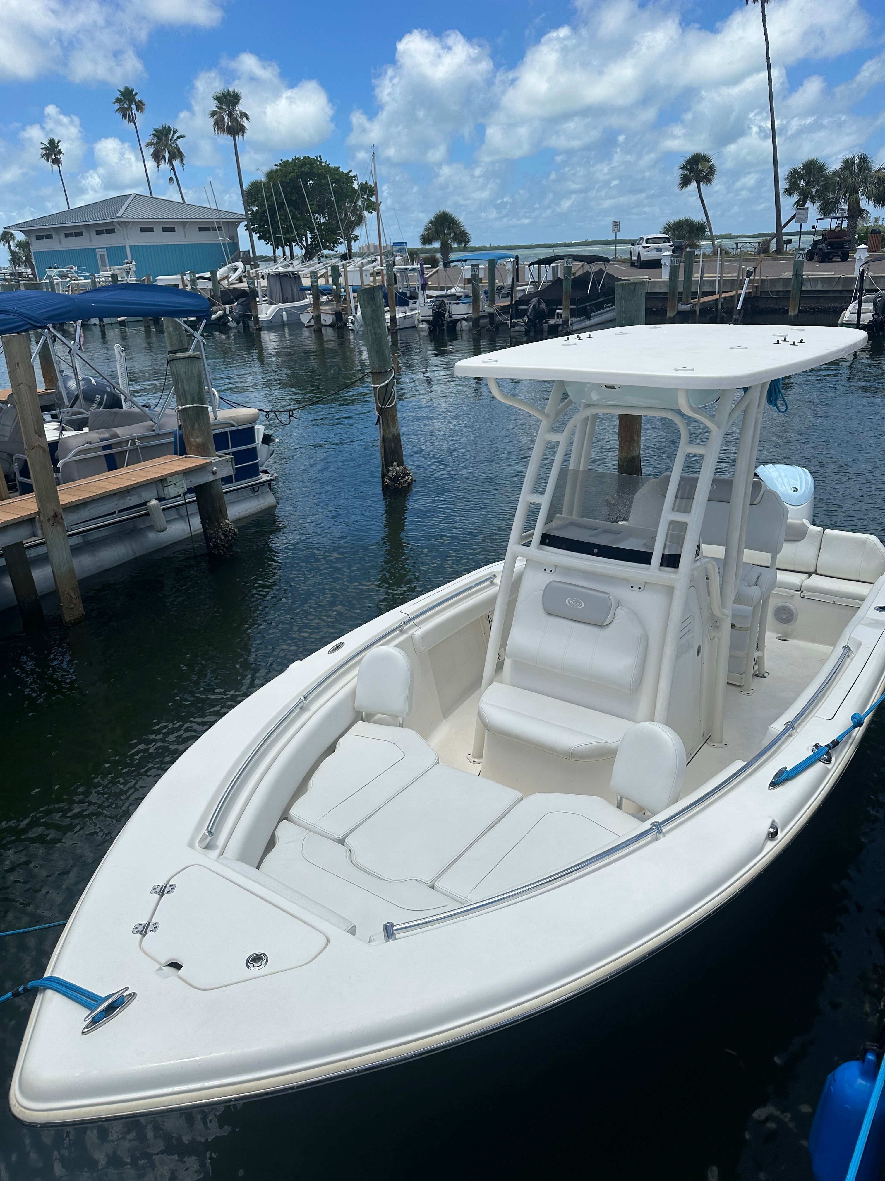 A white boat is docked in a calm marina with palm trees in the background.