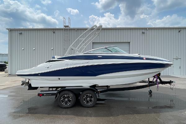 2023 Crownline E235 boat on trailer, parked outside a warehouse under cloudy sky.