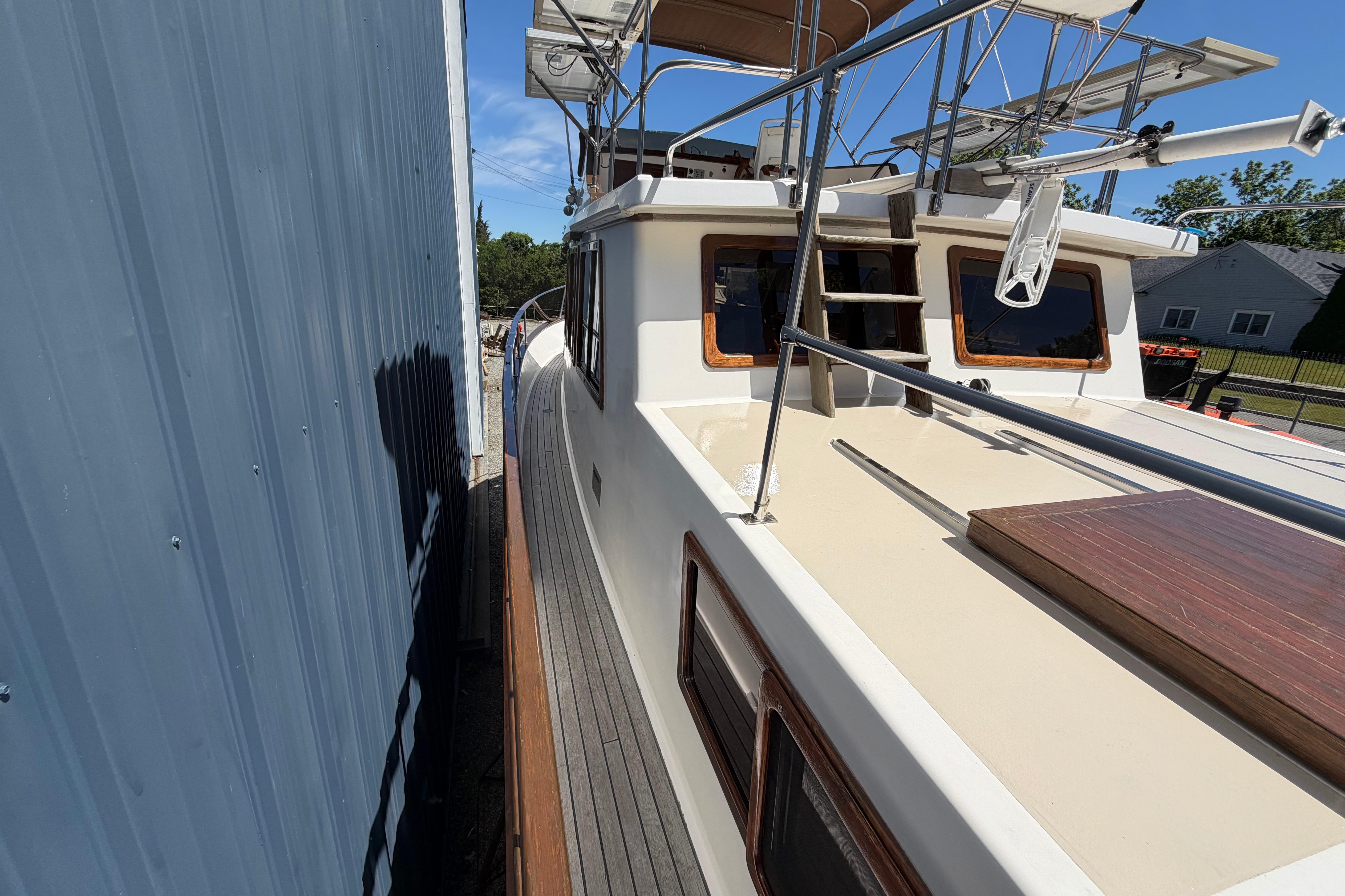 1987 Marine Trader 36 yacht docked beside a blue building, showcasing deck and railing.
