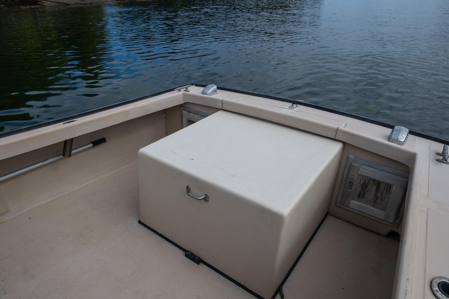 1989 Ellis 24 Open boat interior with storage compartment, docked on calm water.