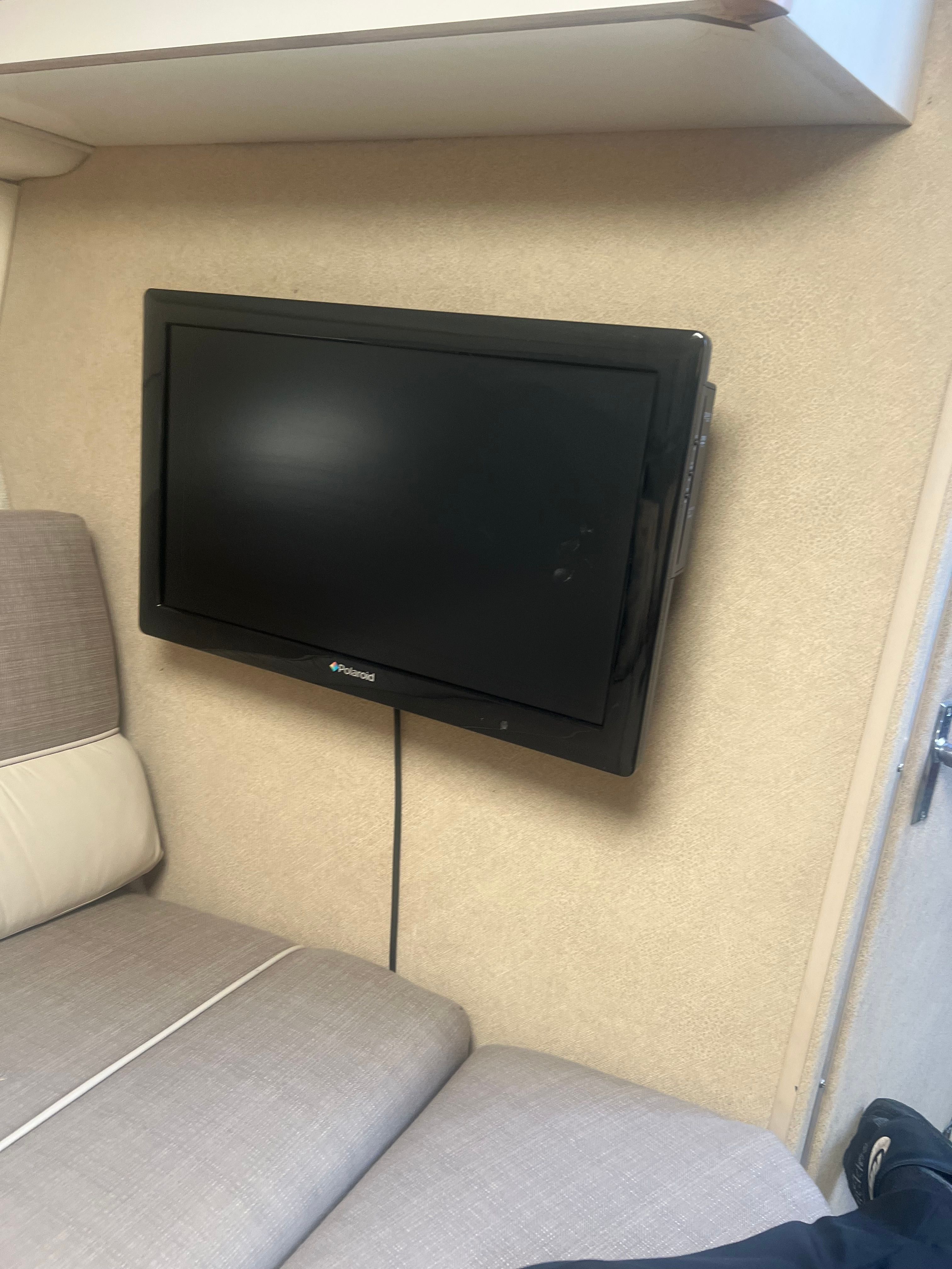 A flat-screen TV is mounted on the wall of a boat cabin, next to a cushioned seating area.
