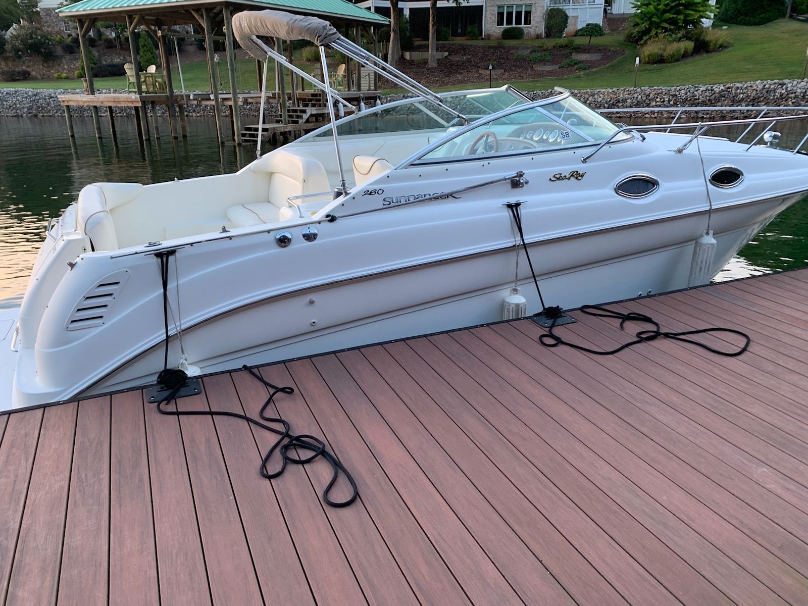 A white 1999 Sea Ray 260 Sundancer boat docked at a wooden pier. It has a sleek design.