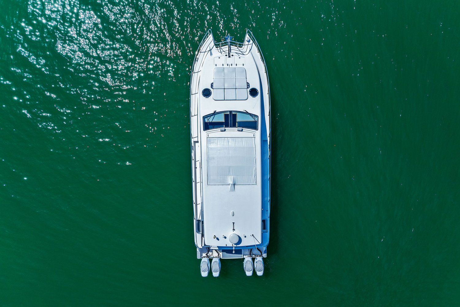 Aerial view of a white catamaran on green water, featuring two outboard engines.