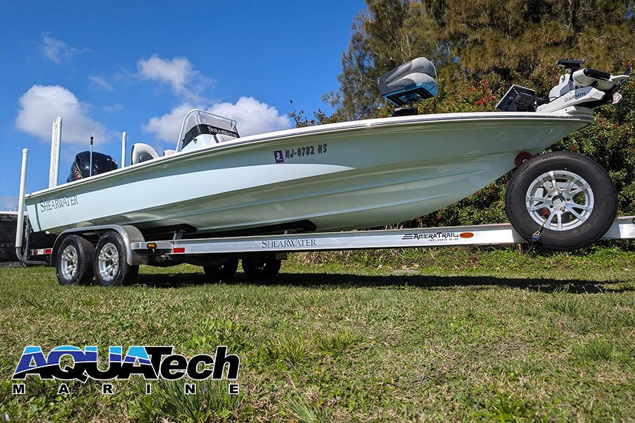 A 2023 ShearWater x22 boat on a trailer, surrounded by grass and trees.