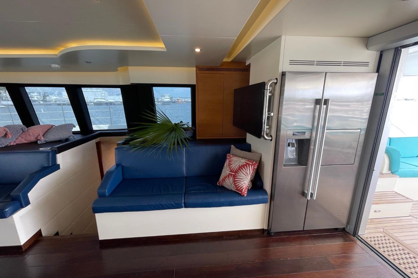 Luxurious yacht interior with blue seating, modern fridge, and ocean view windows, Serenity 64, 2018.