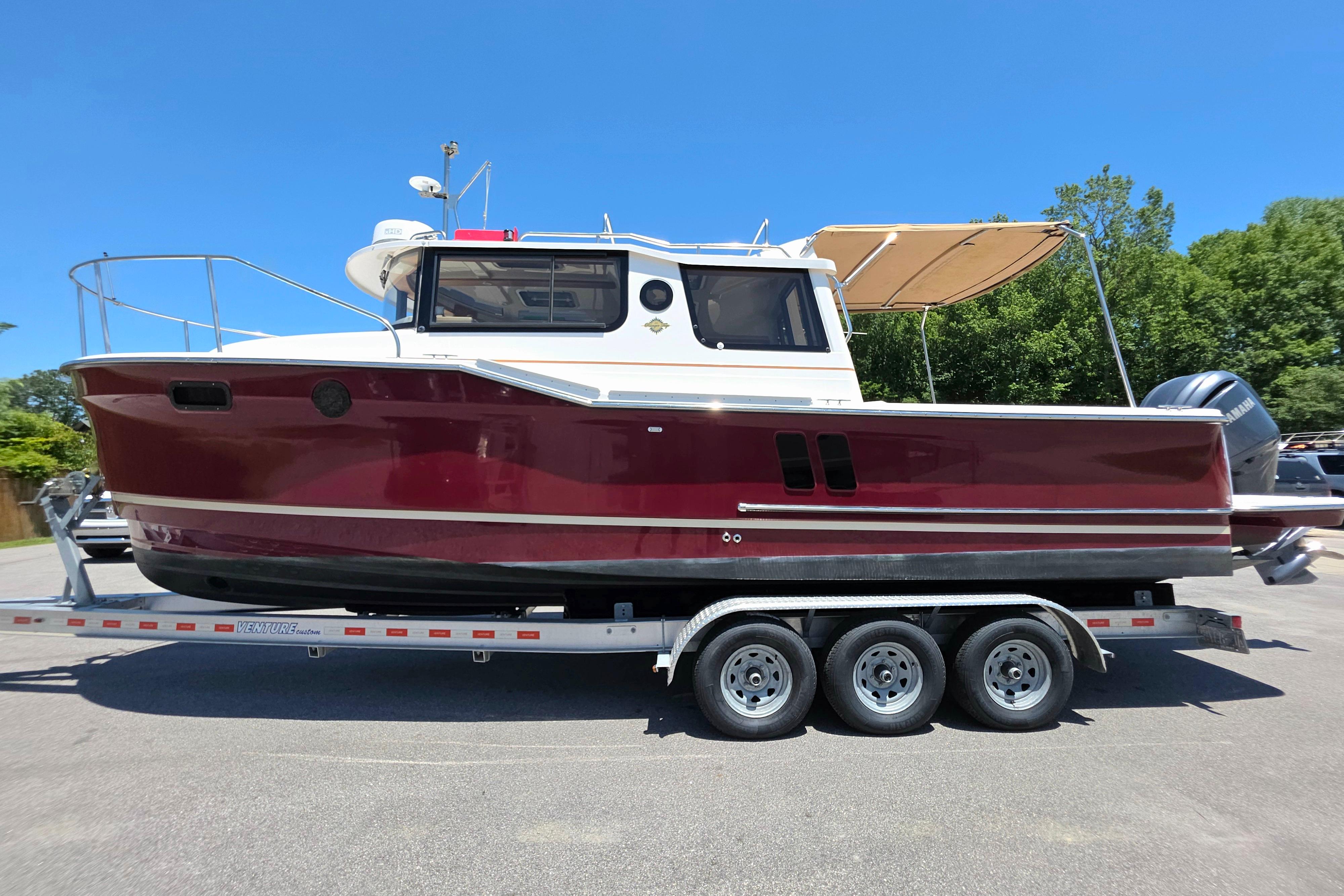 2021 Ranger Tug R27 boat on trailer, red hull, parked outdoors.