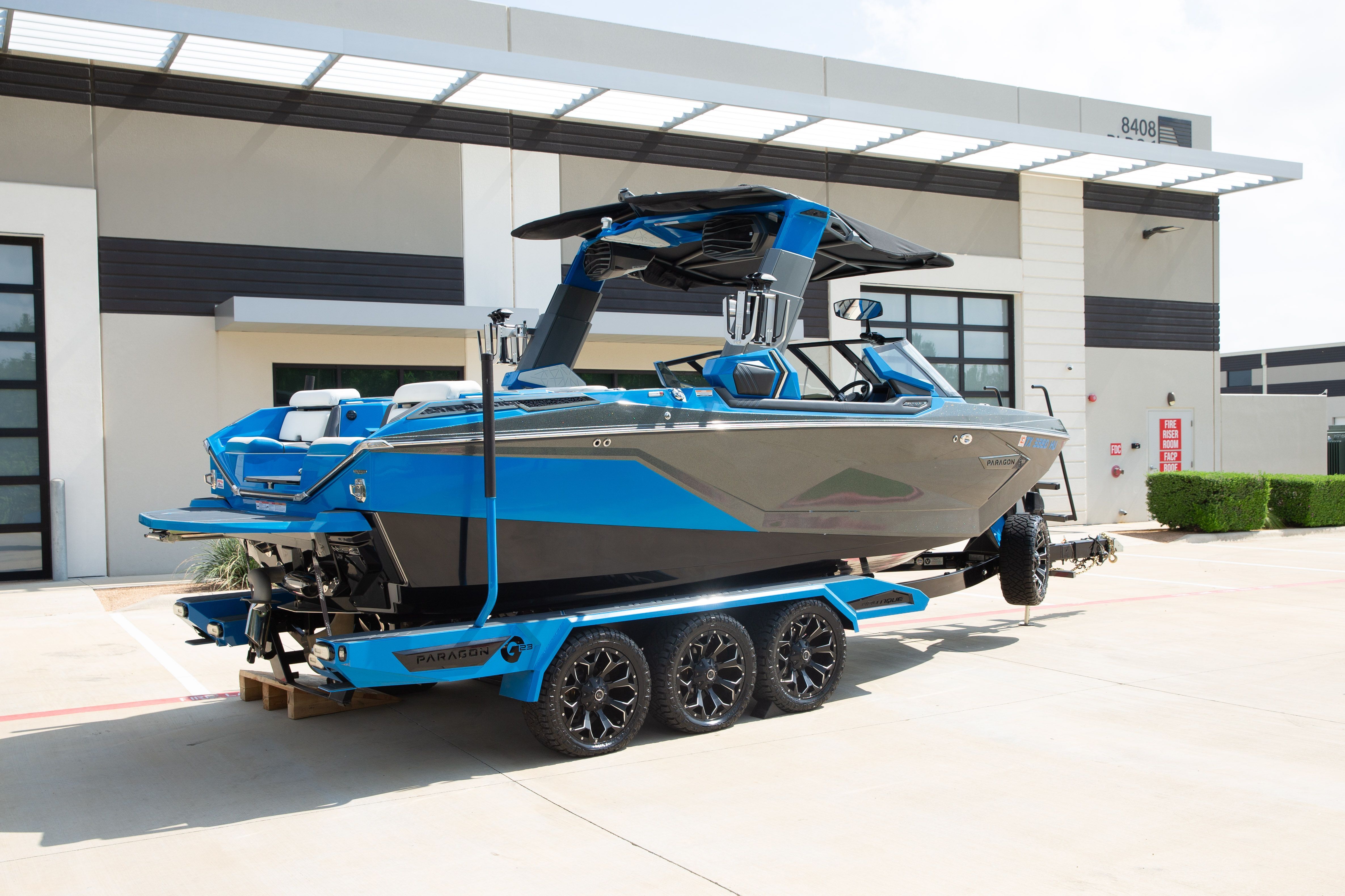 A blue and gray boat on a trailer in front of a modern building.