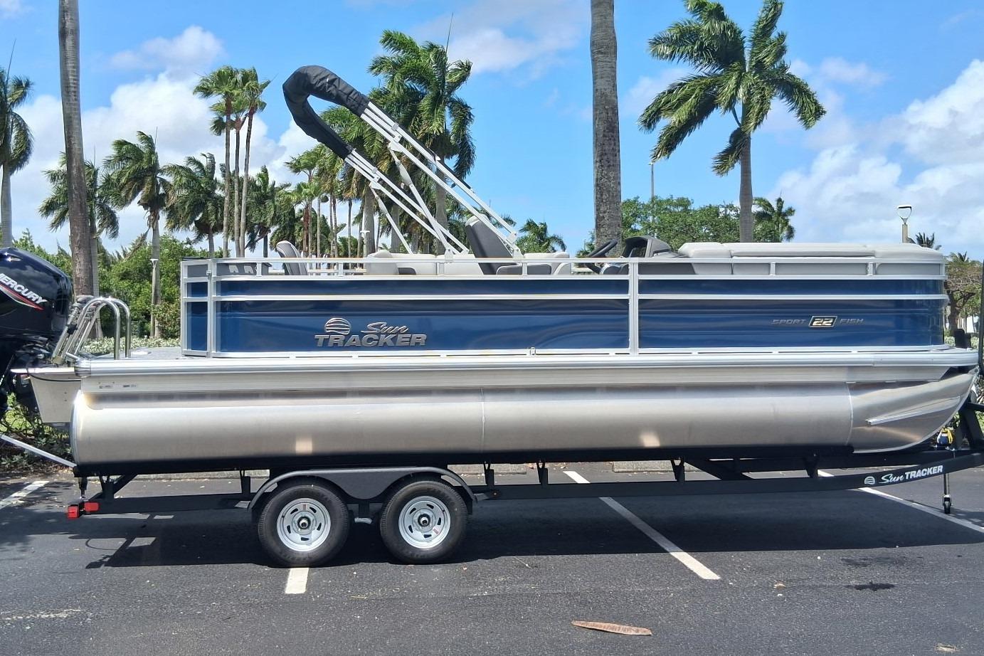 2026 Sun Tracker SportFish 22 DLX pontoon boat on trailer, parked with palm trees in background.