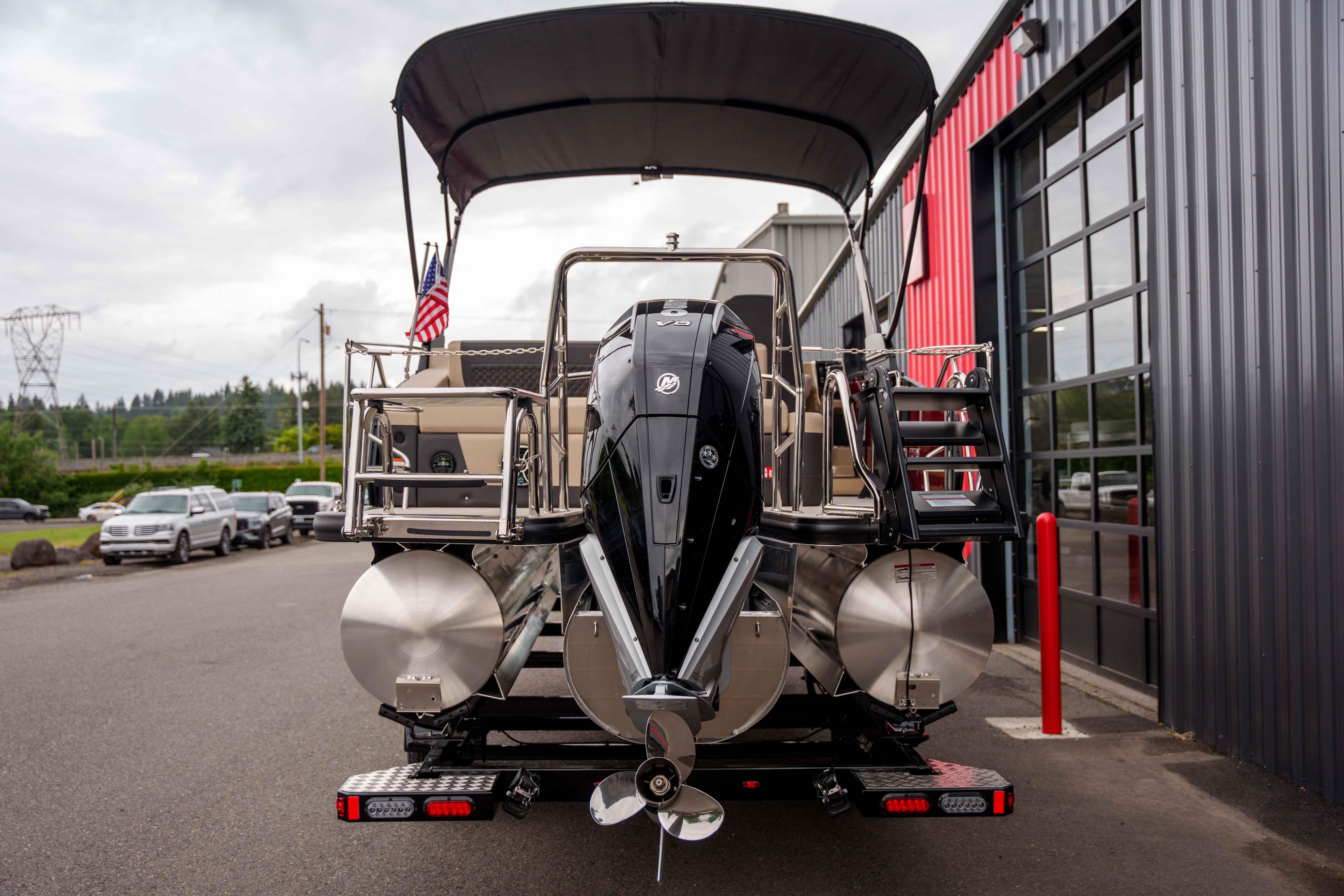 2026 Harris Sunliner 230 pontoon boat with outboard motor, parked near a modern building.