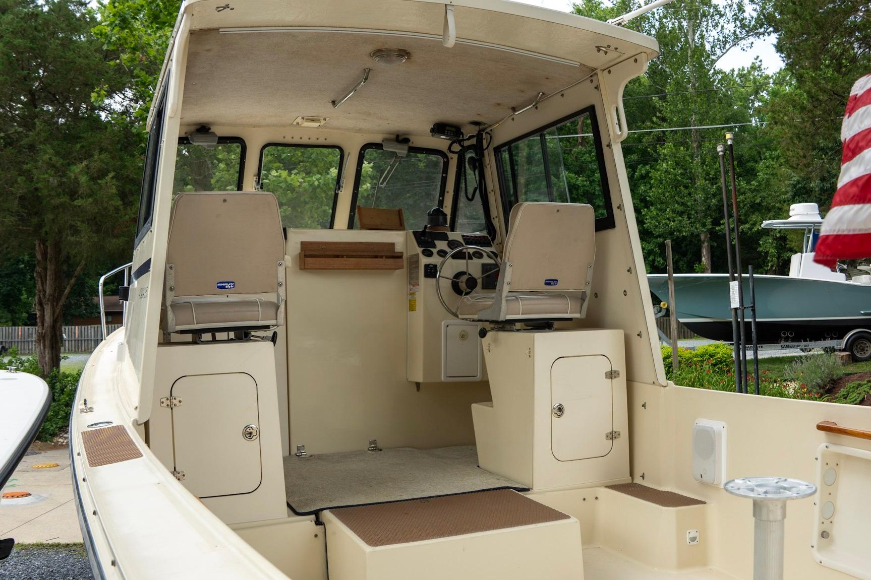 2006 Atlas Boat Works Acadia 25 interior with helm and seating, surrounded by lush greenery.