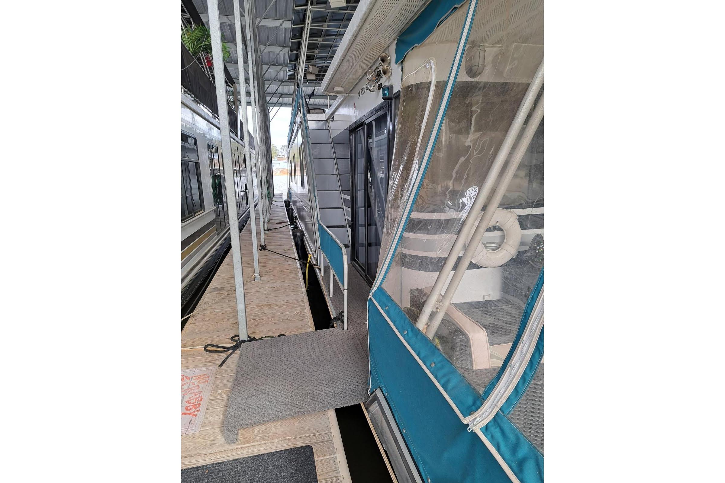 1990 Sumerset 16 x 70 houseboat docked, featuring blue canvas and clear panels.