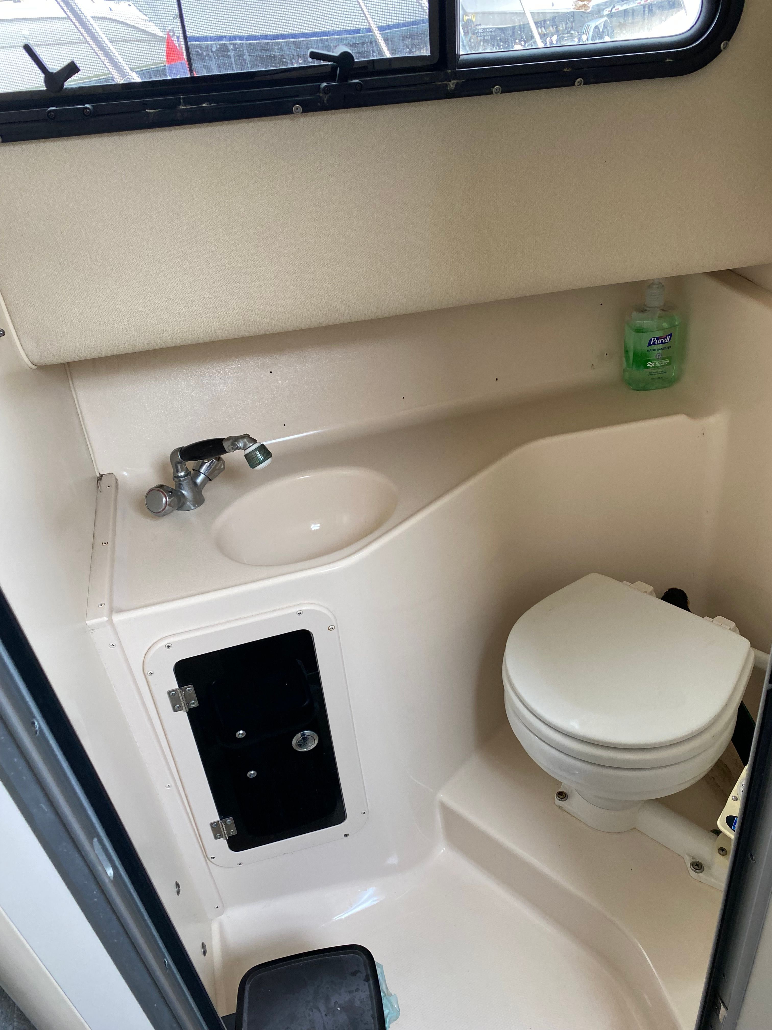 The image shows a small bathroom on a boat with a toilet, sink, and soap dispenser.