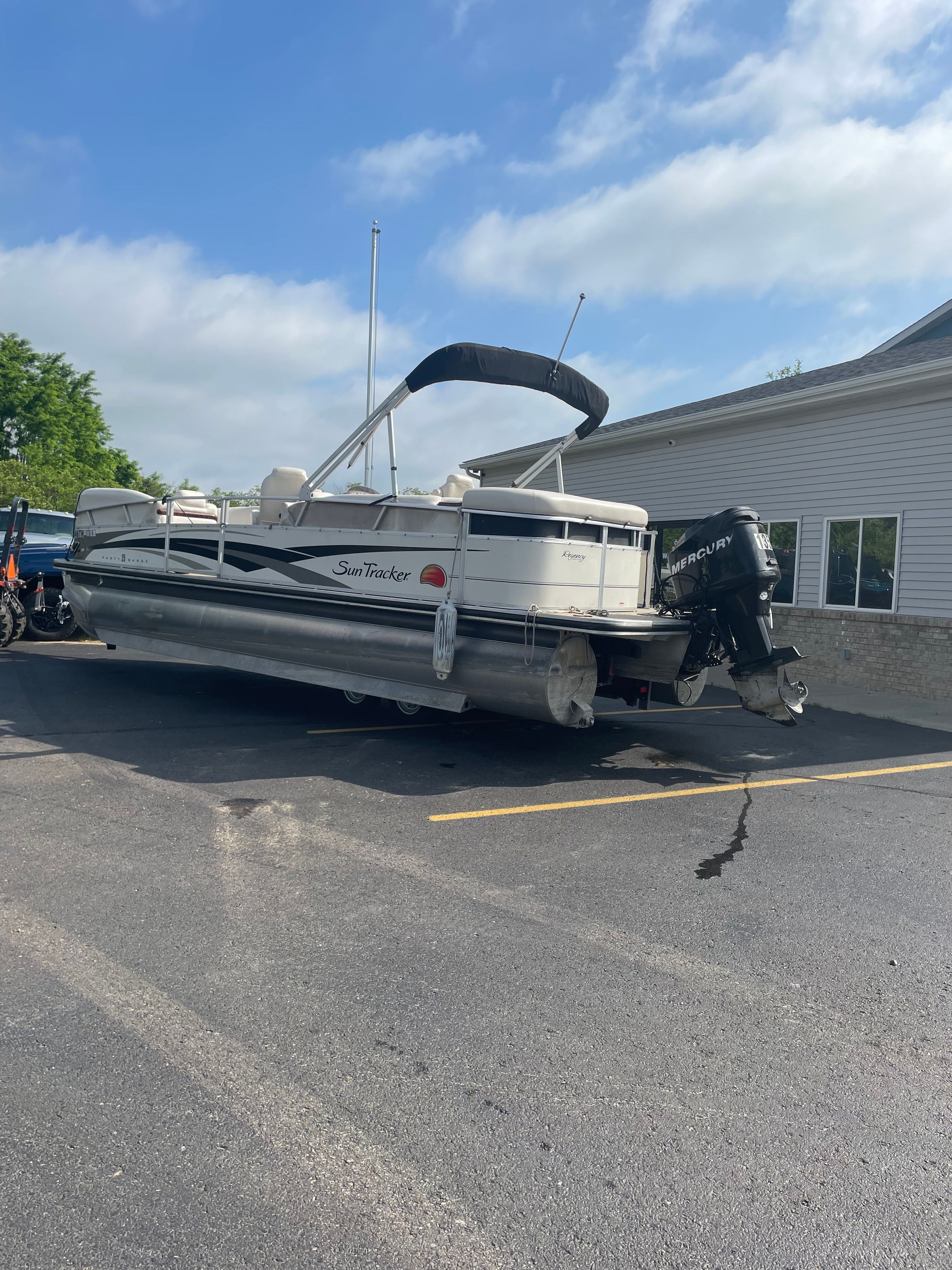 A Sun Tracker Party Barge 25 Regency Edition boat is parked on a lot.