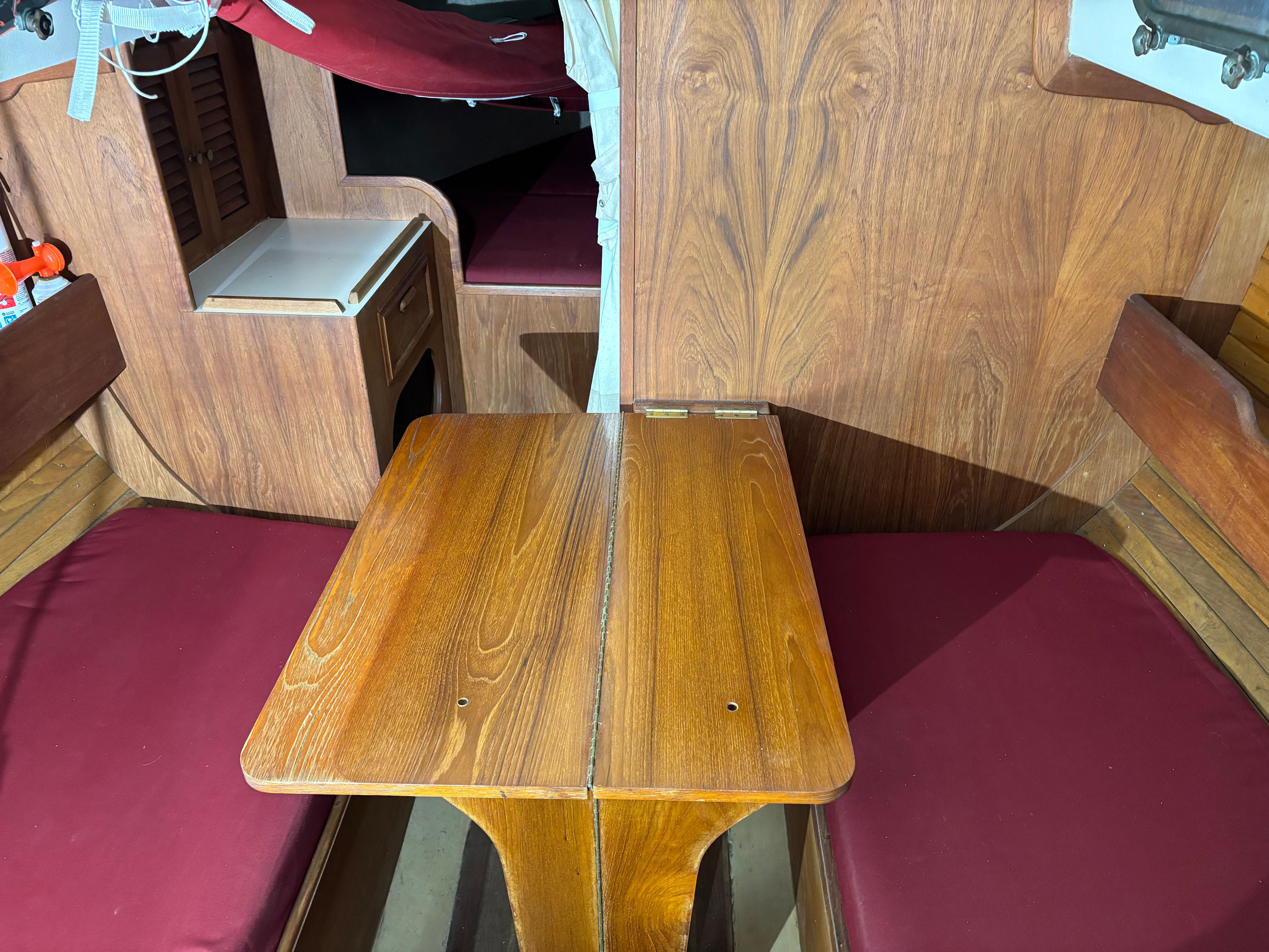 Interior of a Cape Dory 26 yacht, wooden table and red cushions.