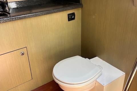 2024 Bracewell 25 boat interior bathroom with compact toilet and wooden paneling.