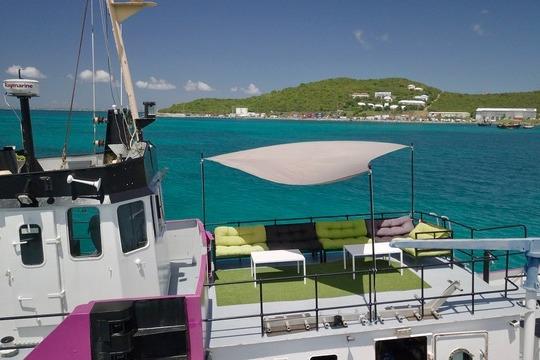 A 1970 Custom CD Holmes Clovelly Class Tender Fleet with deck seating, anchored near a scenic coastline.