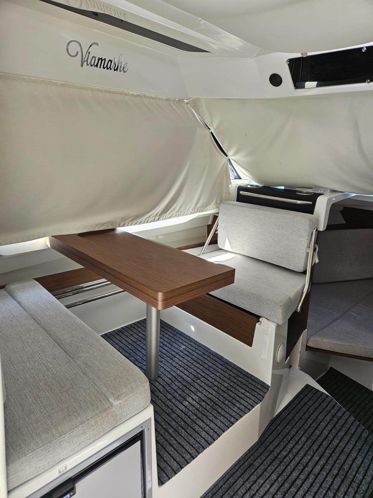 2023 Jeanneau NC795 S2 interior with dining area, wooden table, and cushioned seating.