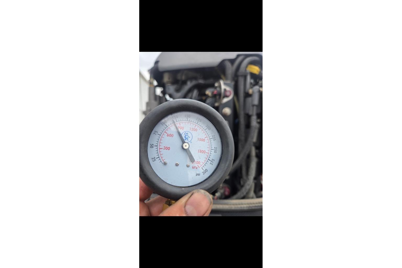Hand holding pressure gauge near Tracker Pro Team 190 TX engine, 2015 model.