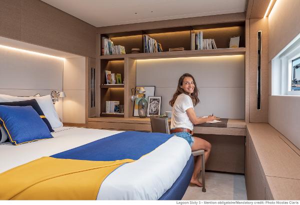 A woman in a modern cabin of a 2025 Lagoon SIXTY 5 yacht, sitting at a desk.