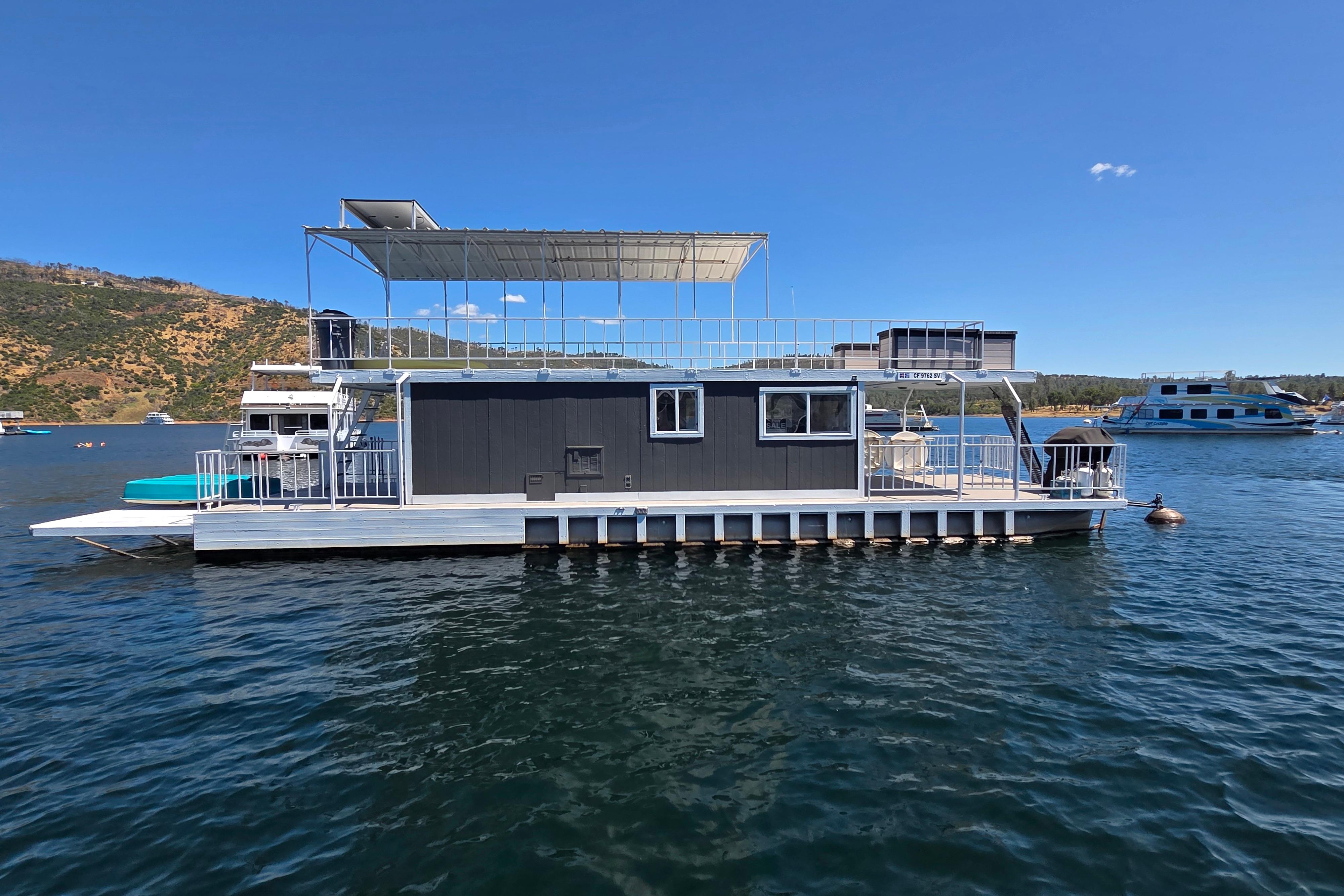 Custom 2007 houseboat on a lake with clear blue skies and distant hills.