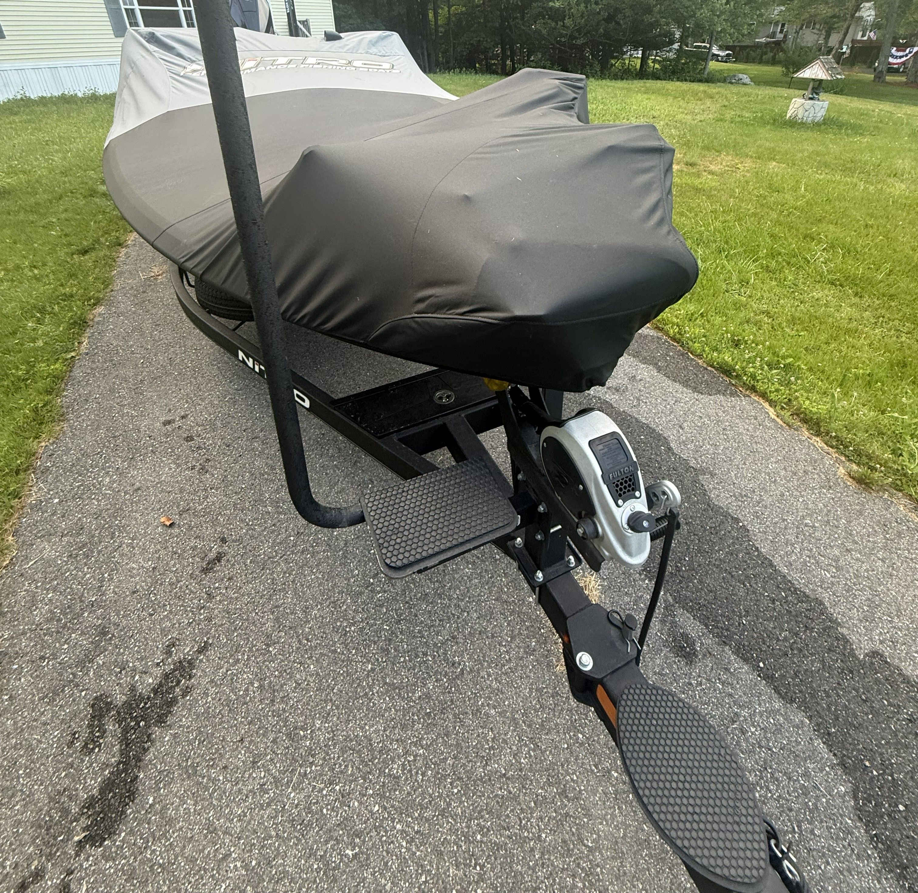 A covered boat on a trailer is parked on a driveway.