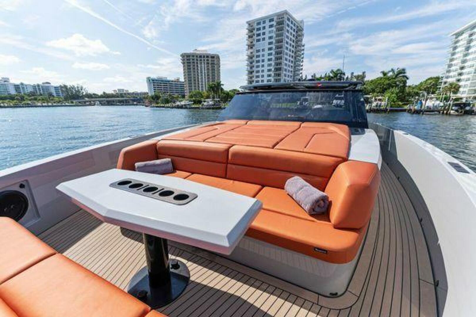 Luxurious 2021 Vanquish VQ58 yacht with orange seating, docked near waterfront buildings.