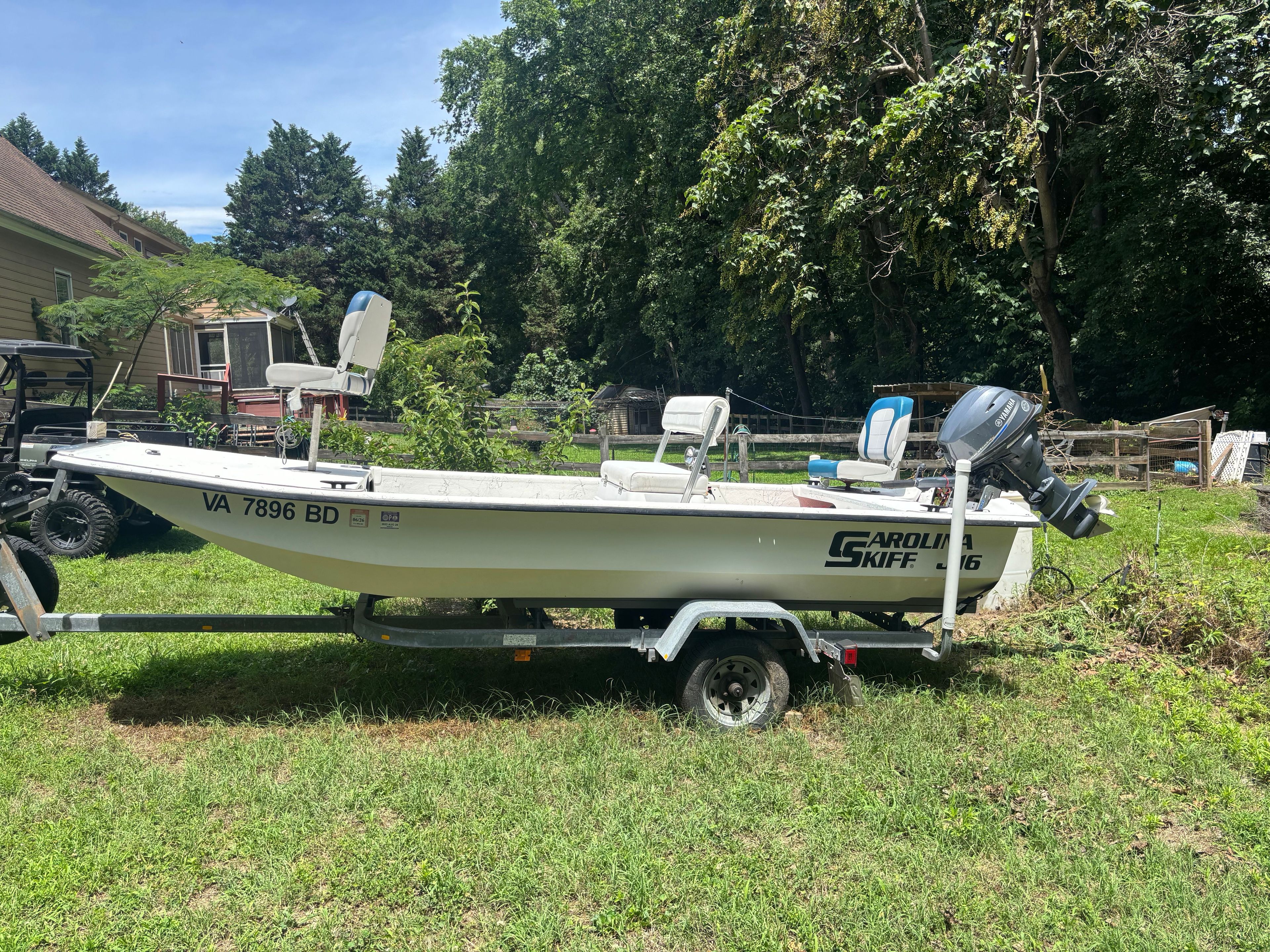 A 2004 Carolina Skiff J16 boat on a trailer in a yard, surrounded by trees.