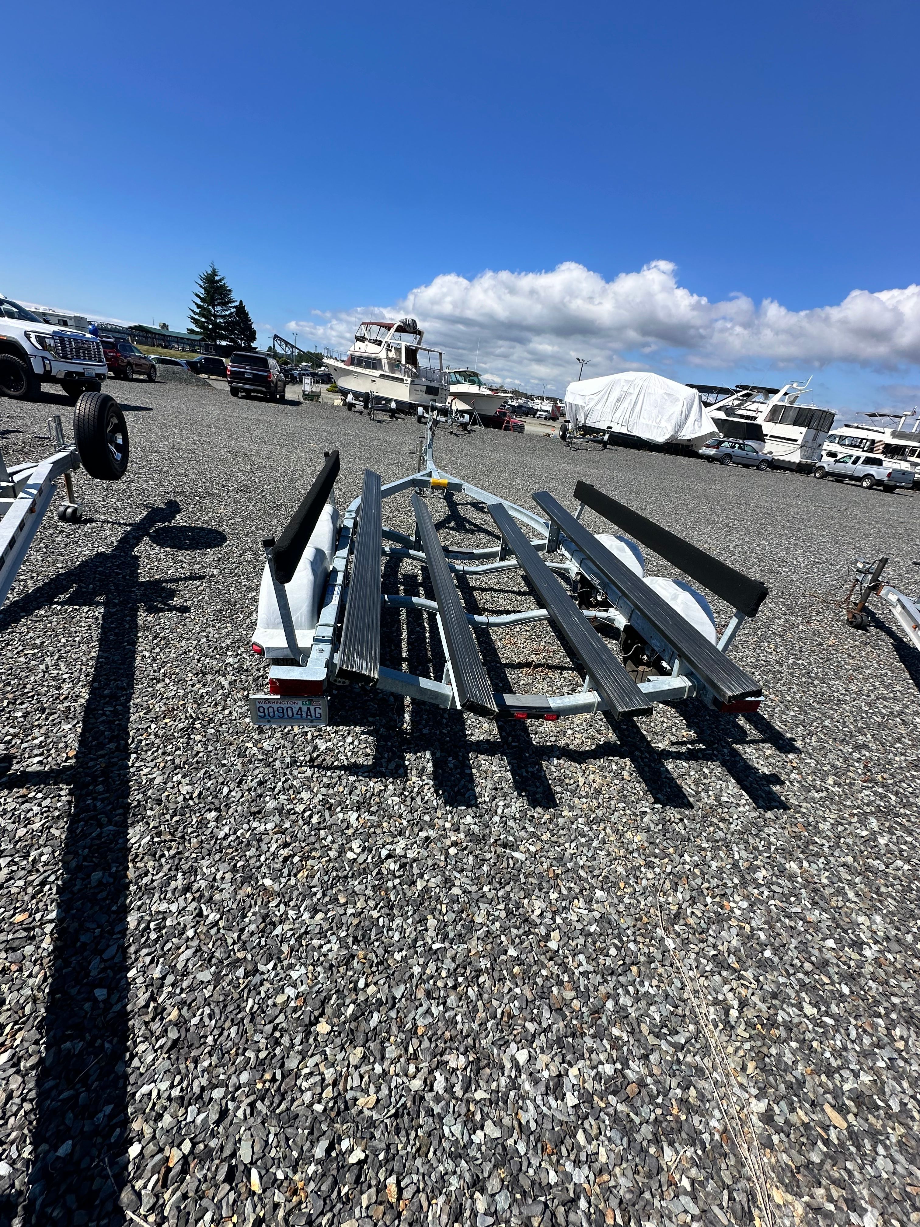 Boat trailer on a gravel lot with several boats in the background.