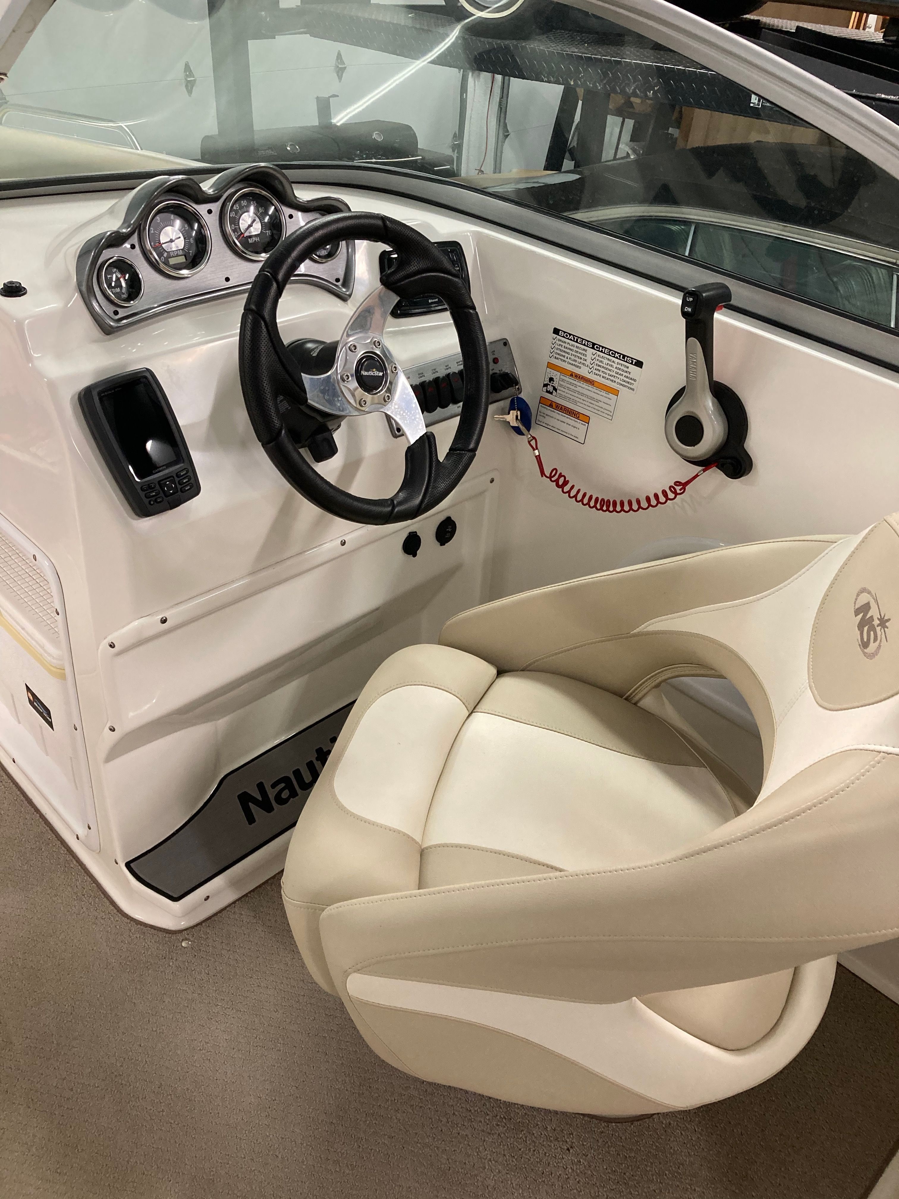 Interior view of a boat with a steering wheel and beige seat.