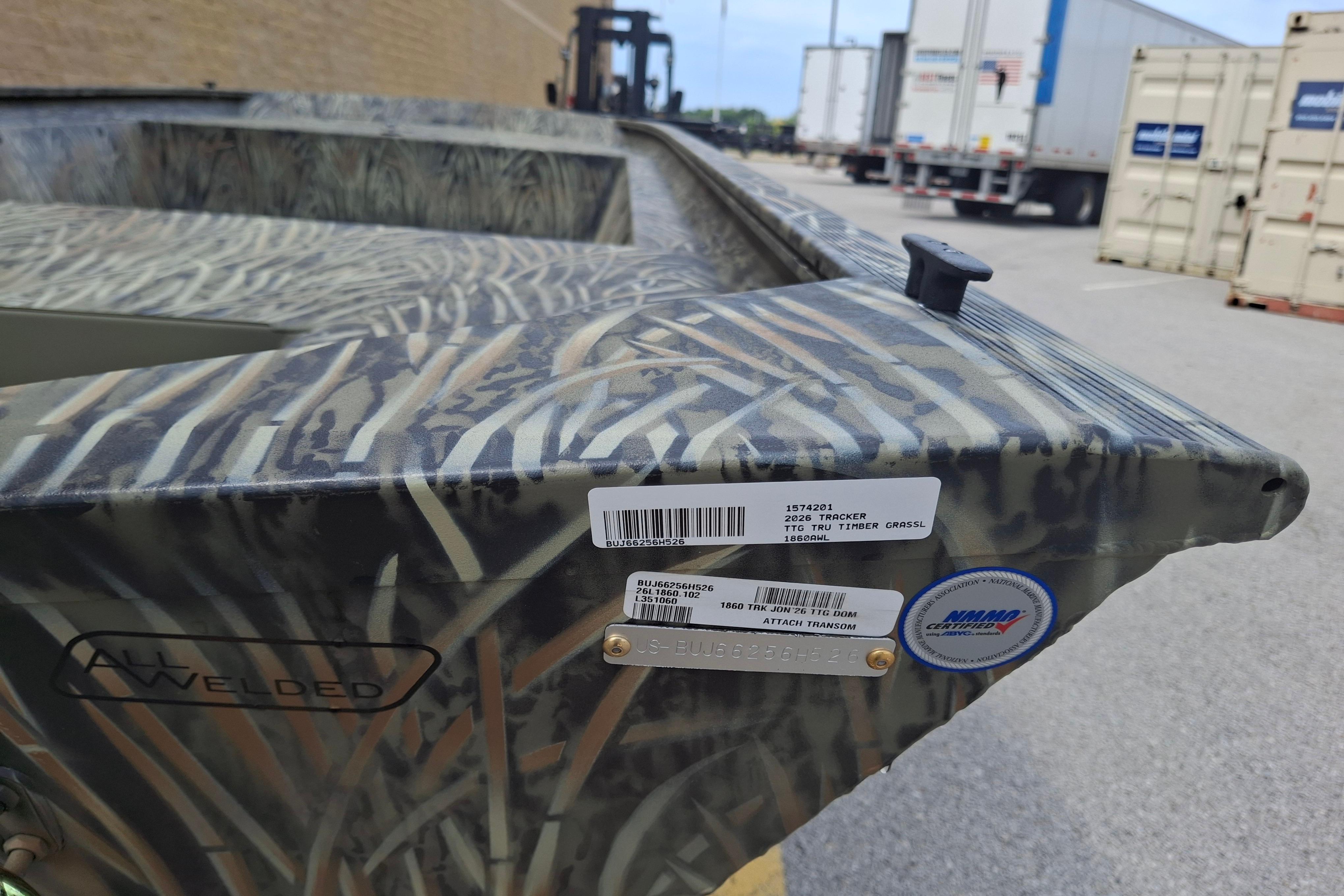 2026 Tracker Grizzly 1860 Utility boat with camo pattern, parked near shipping containers.