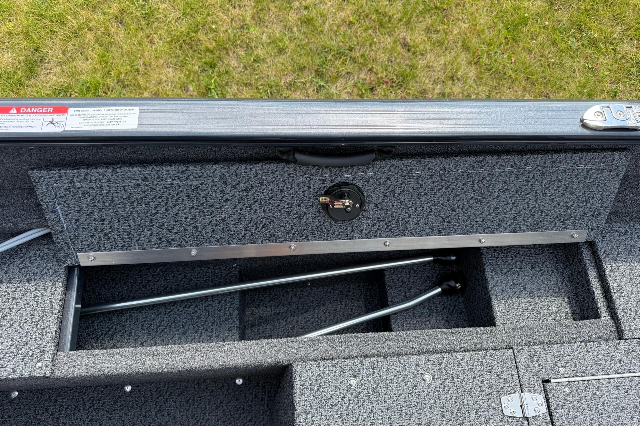 2027 Lund 1650 Rebel XL SS boat storage compartment with metal rods, open on grassy background.