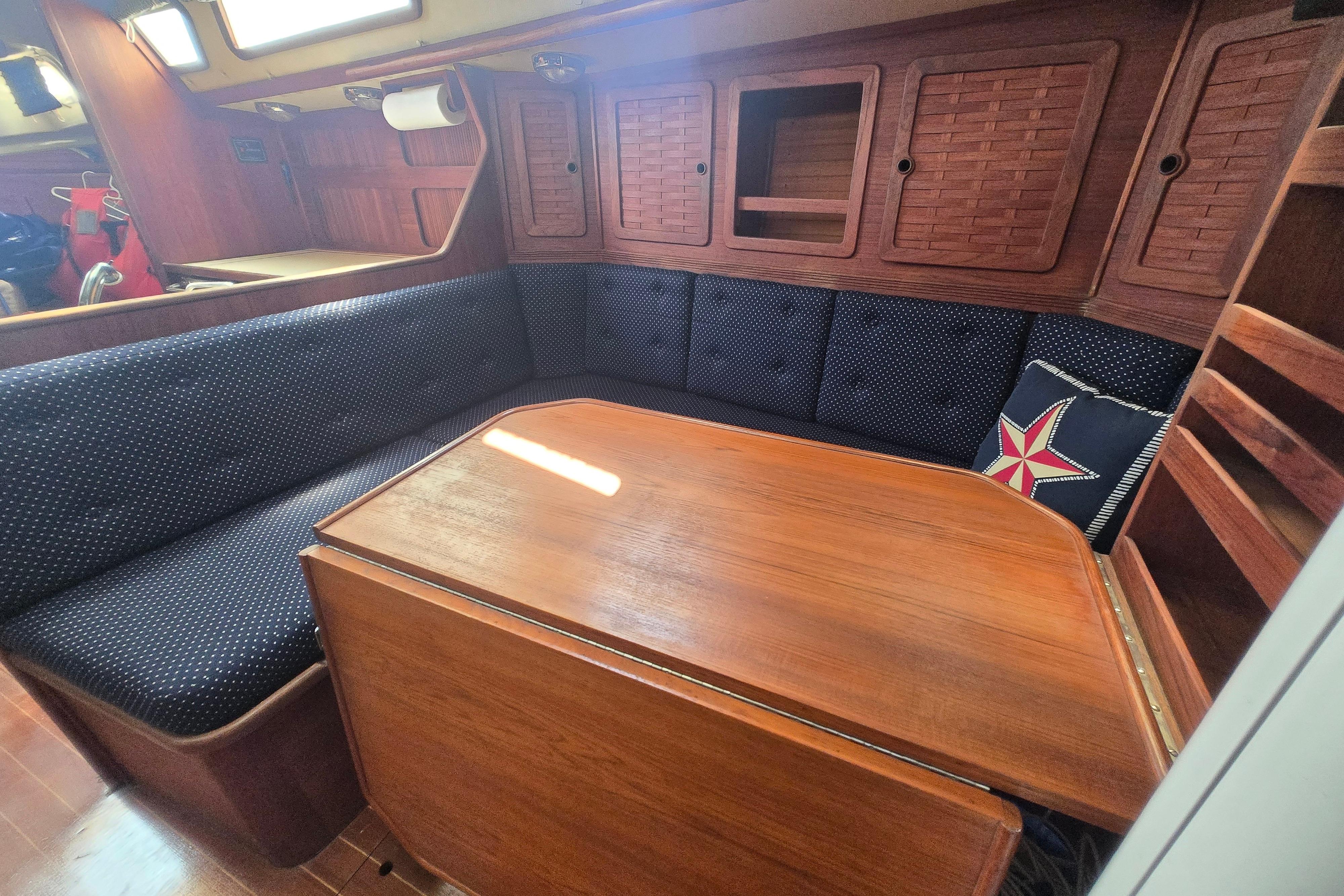 1988 Sabre 38 yacht interior with wooden table, cushioned seating, and star-patterned pillow.