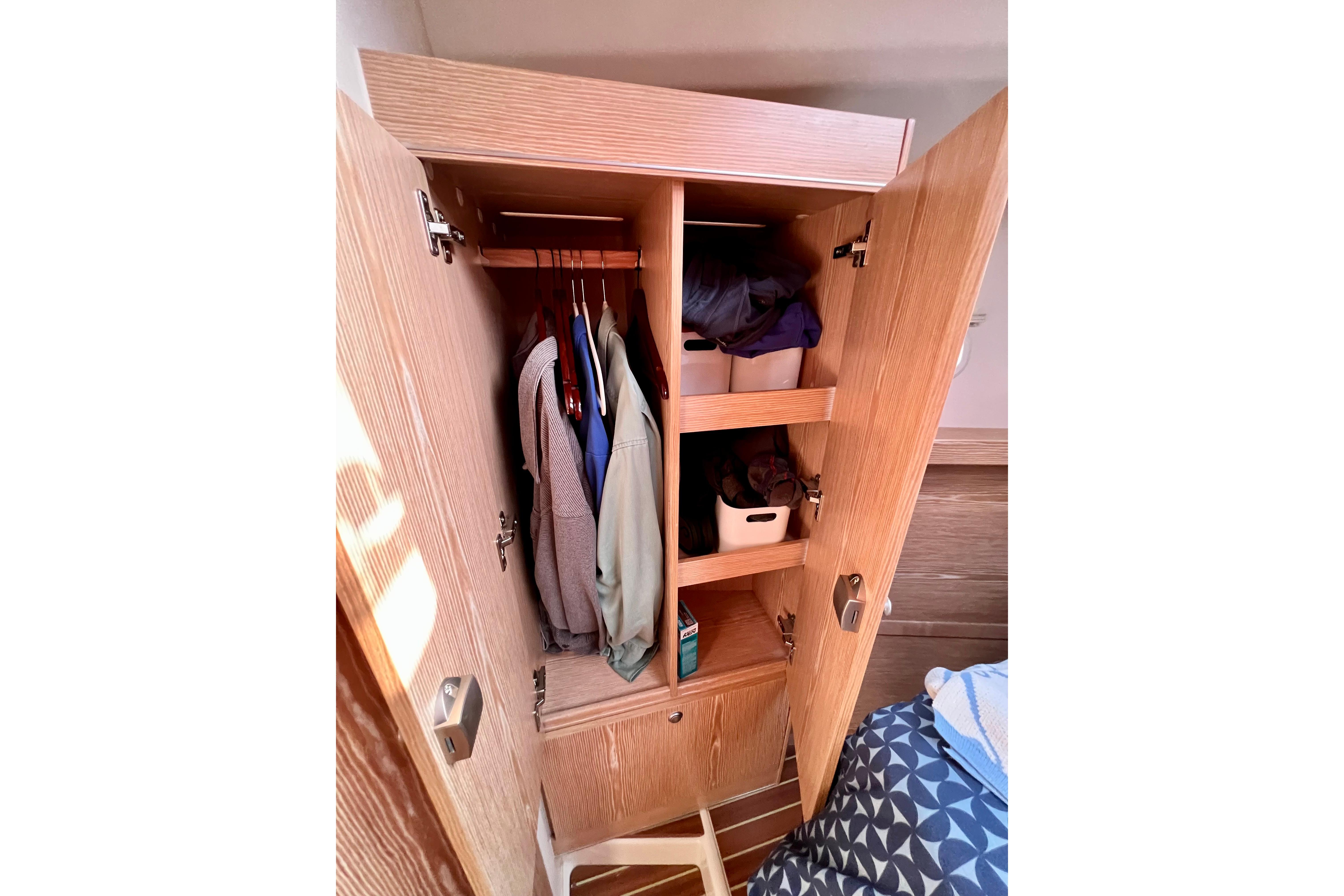 Wooden wardrobe interior on a 2016 Hanse 455 yacht, with clothes and storage bins.