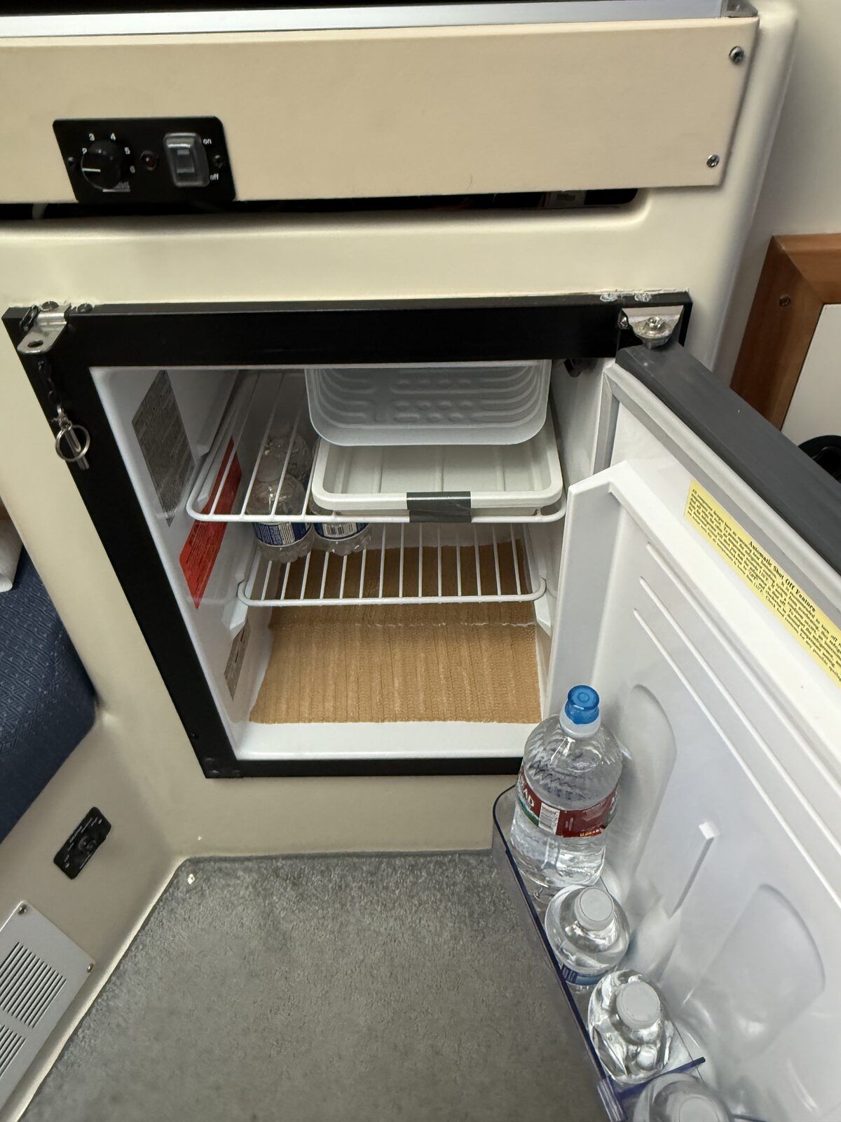 A small fridge on a boat with water bottles in the door.