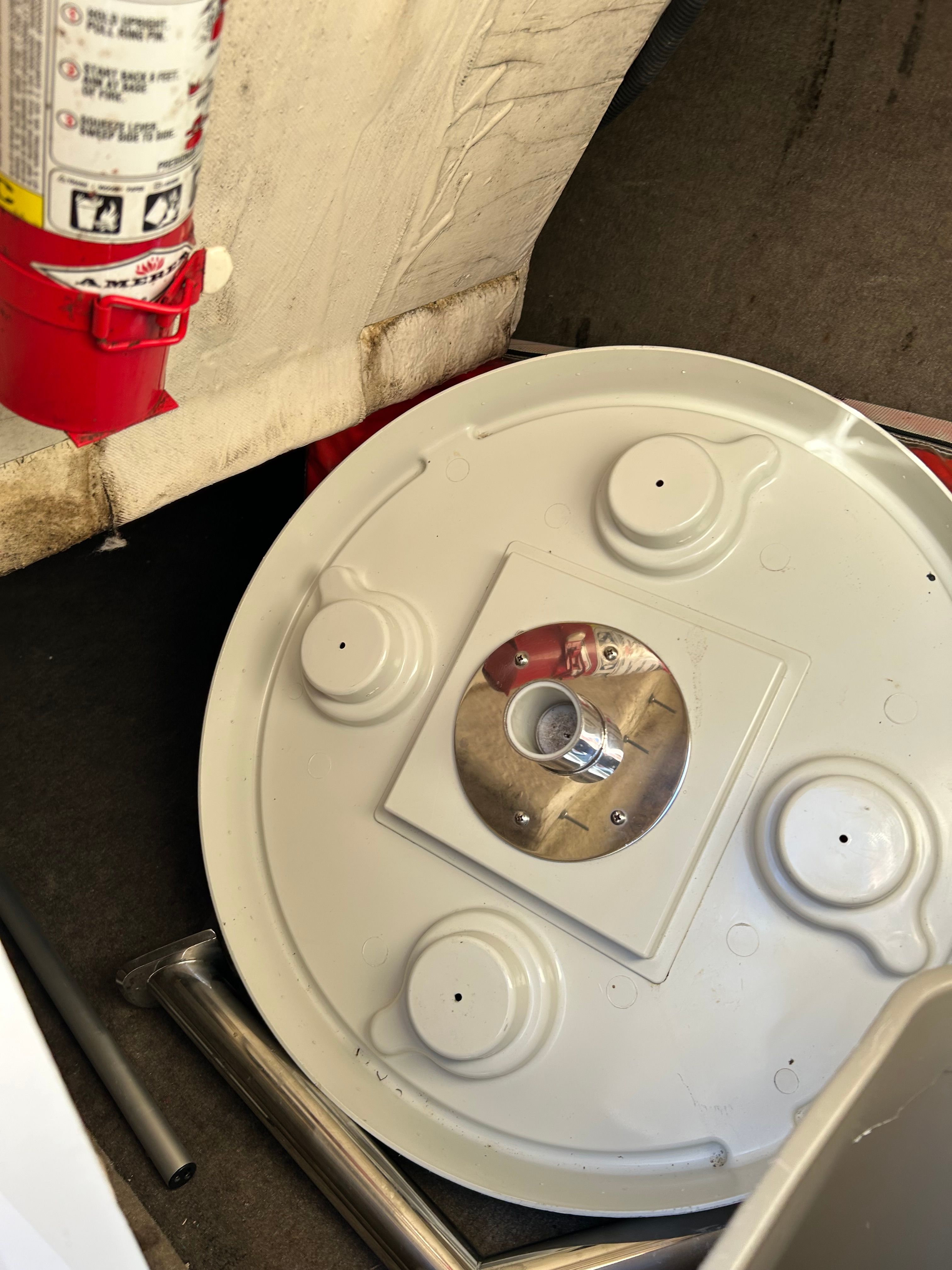 A round, white cover with metal fittings lies on a boat floor next to a fire extinguisher.
