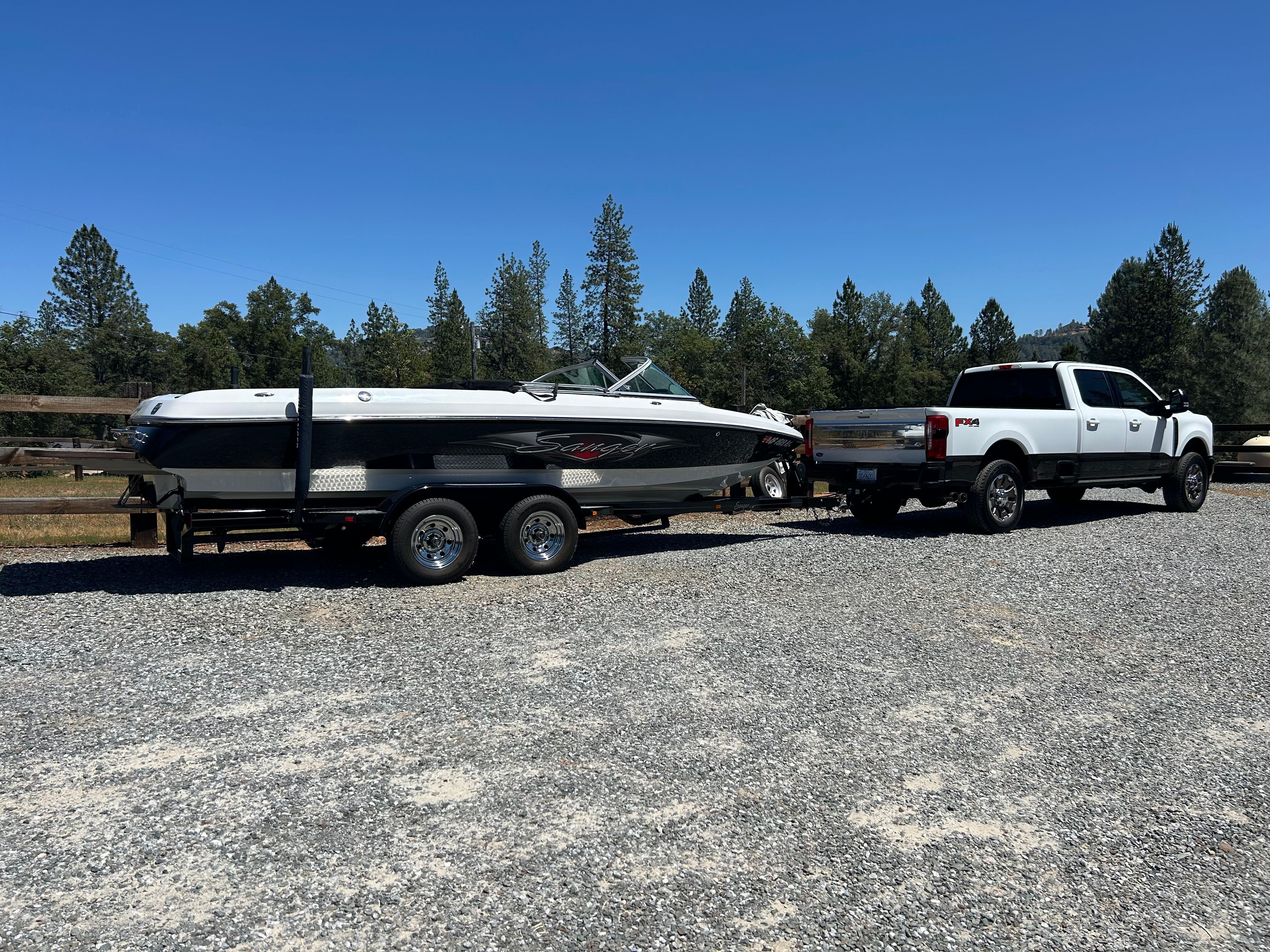 A 2007 Sanger boat is towed by a white pickup truck on a gravel path.