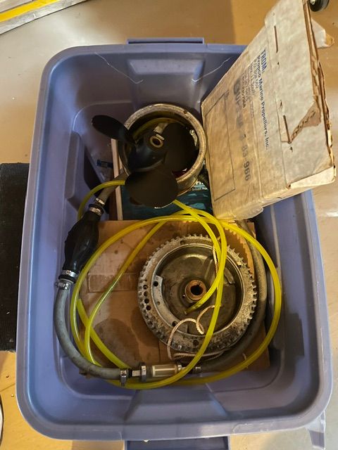 A plastic container with boat parts, including a propeller and hoses.